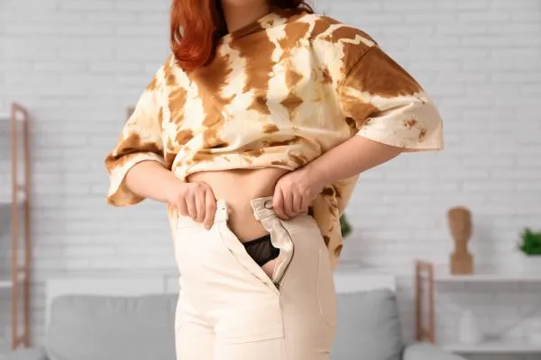 Image of woman trying to do her trousers up after pregnancy weight gain Midlands